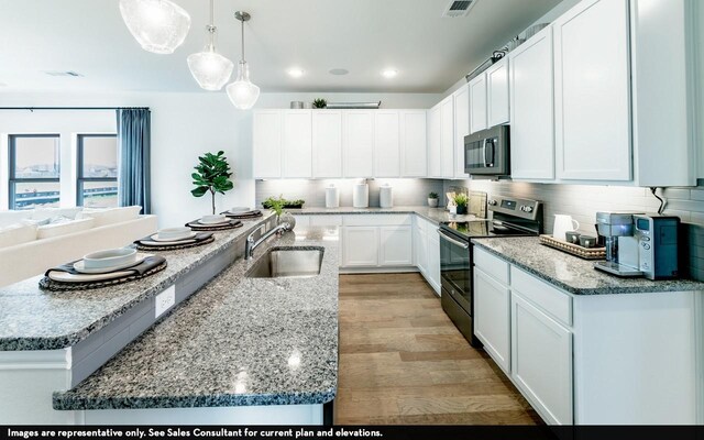 kitchen featuring electric range, sink, decorative light fixtures, a center island with sink, and white cabinets