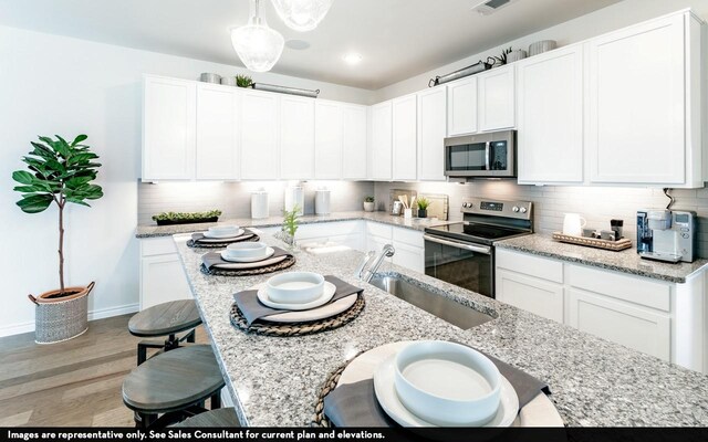 kitchen featuring appliances with stainless steel finishes, sink, wood-type flooring, white cabinets, and hanging light fixtures