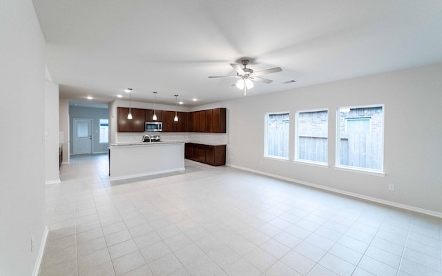 kitchen with dark brown cabinetry, ceiling fan, light tile patterned flooring, pendant lighting, and a kitchen island with sink