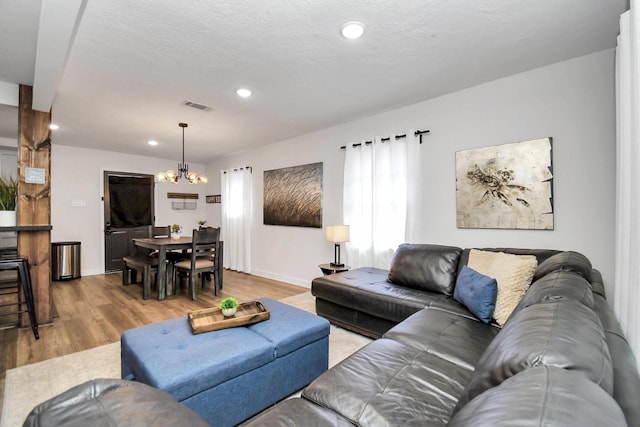 living room featuring a textured ceiling, light hardwood / wood-style floors, vaulted ceiling, and a notable chandelier