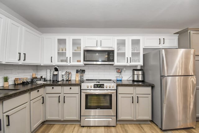 kitchen with dark stone countertops, decorative backsplash, light hardwood / wood-style flooring, and appliances with stainless steel finishes