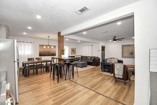 dining space with ceiling fan with notable chandelier, wood-type flooring, and a textured ceiling