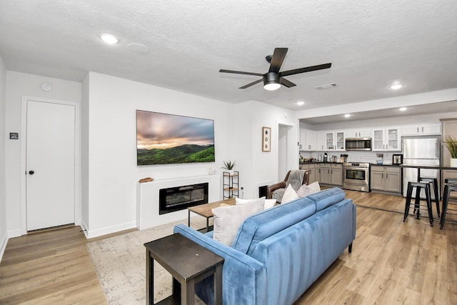 living room featuring ceiling fan, light hardwood / wood-style floors, and a textured ceiling