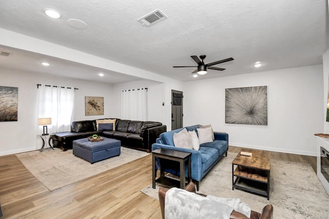 living room with light wood-type flooring, a textured ceiling, and ceiling fan