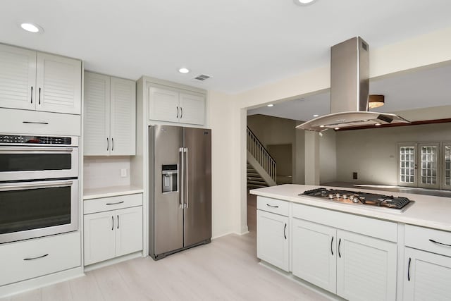 kitchen with backsplash, island range hood, white cabinets, and appliances with stainless steel finishes