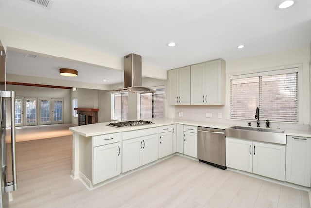 kitchen with island exhaust hood, decorative backsplash, kitchen peninsula, stainless steel appliances, and sink