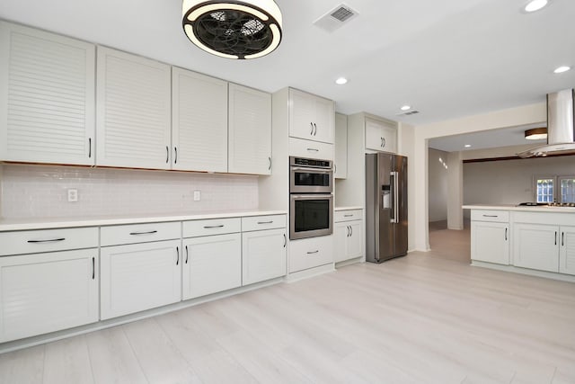 kitchen featuring tasteful backsplash, white cabinetry, stainless steel appliances, and wall chimney range hood