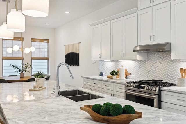 kitchen with high end range, sink, decorative backsplash, light stone countertops, and white cabinetry