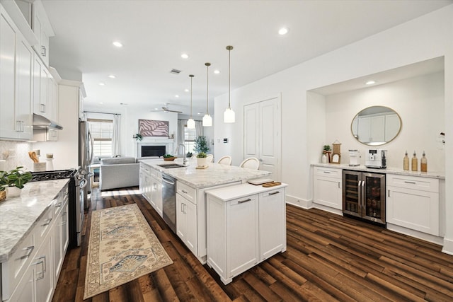 kitchen featuring decorative light fixtures, wine cooler, a kitchen island with sink, and white cabinetry