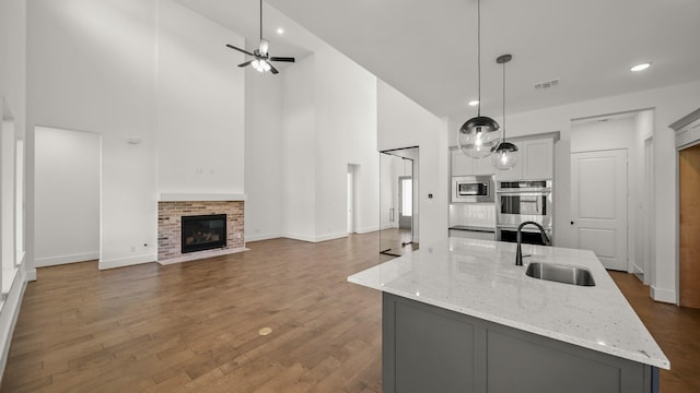 kitchen featuring gray cabinetry, a high ceiling, light stone countertops, decorative light fixtures, and stainless steel appliances