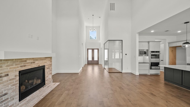 unfurnished living room with wood-type flooring, an inviting chandelier, a brick fireplace, and a high ceiling