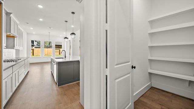 kitchen featuring stainless steel gas stovetop, a kitchen island with sink, hanging light fixtures, hardwood / wood-style flooring, and white cabinetry