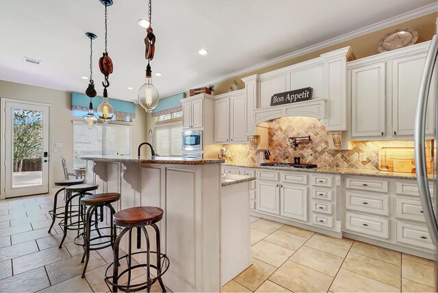 kitchen featuring hanging light fixtures, a wealth of natural light, white cabinetry, and a kitchen island with sink