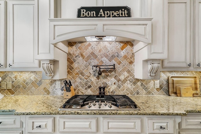 kitchen with tasteful backsplash, white cabinetry, stainless steel gas stovetop, and light stone counters