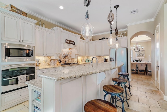 kitchen with stainless steel appliances, crown molding, pendant lighting, a center island with sink, and white cabinetry