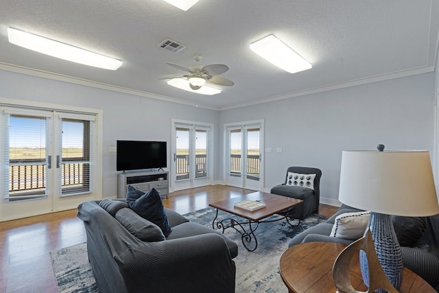 living room featuring ceiling fan, ornamental molding, a textured ceiling, and light wood-type flooring