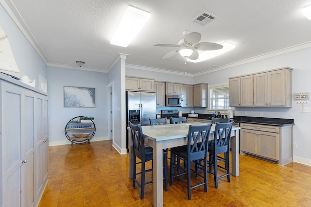 kitchen featuring ceiling fan, crown molding, a textured ceiling, a kitchen island, and appliances with stainless steel finishes