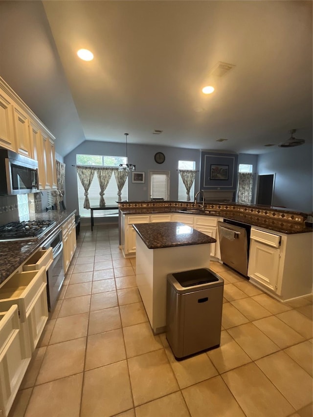 kitchen with kitchen peninsula, appliances with stainless steel finishes, light tile patterned floors, decorative light fixtures, and a center island