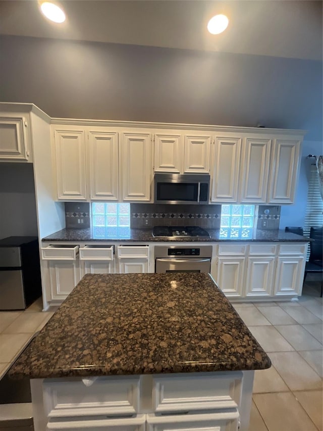 kitchen featuring decorative backsplash, appliances with stainless steel finishes, dark stone countertops, white cabinets, and light tile patterned flooring