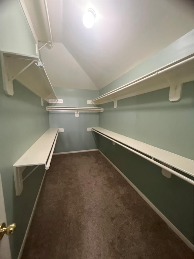 spacious closet with dark colored carpet and vaulted ceiling