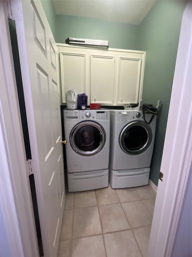 clothes washing area featuring washing machine and dryer, light tile patterned floors, and cabinets