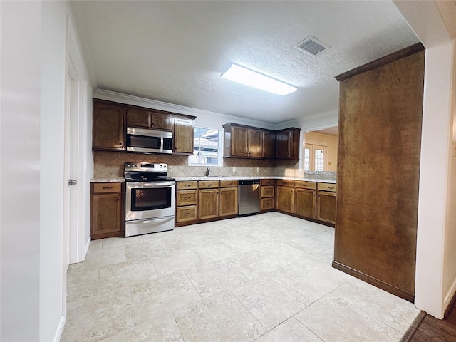 kitchen featuring backsplash, sink, crown molding, a textured ceiling, and appliances with stainless steel finishes