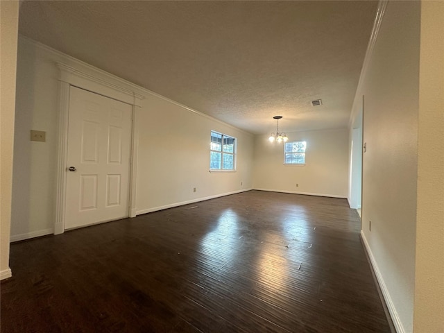 empty room featuring a textured ceiling, dark hardwood / wood-style flooring, an inviting chandelier, and crown molding