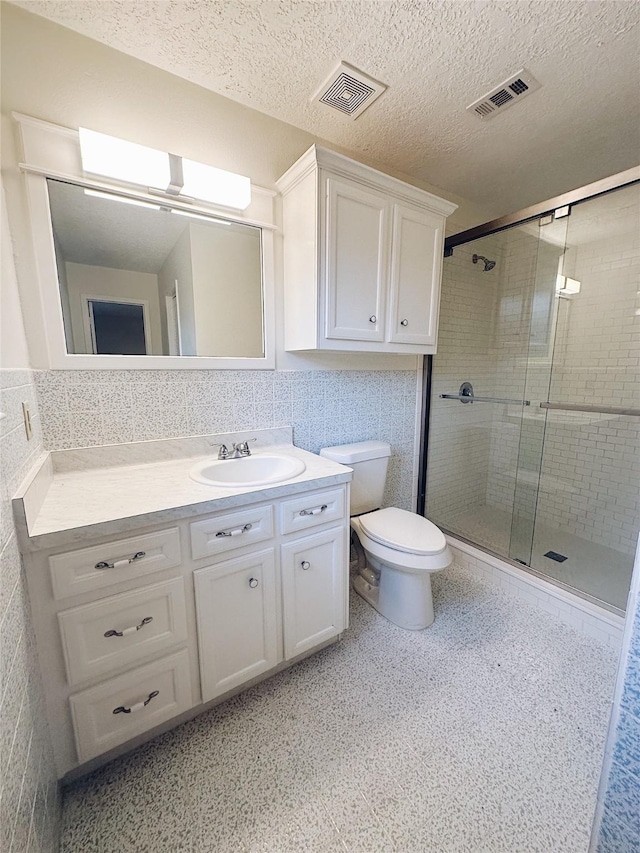 bathroom with vanity, toilet, a textured ceiling, tile walls, and walk in shower