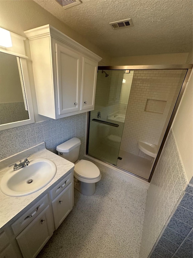 bathroom with a textured ceiling, vanity, tile walls, toilet, and a shower with shower door