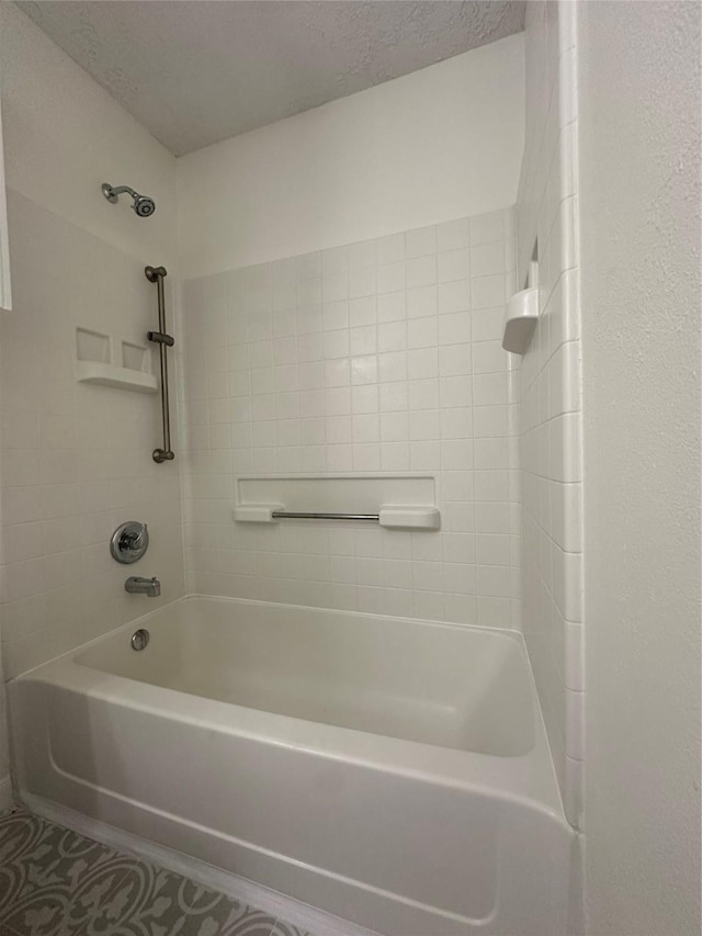 bathroom featuring a textured ceiling and tiled shower / bath