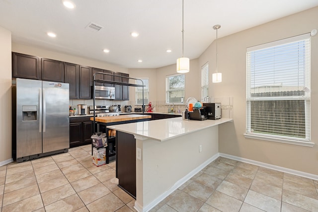 kitchen featuring stainless steel appliances, kitchen peninsula, decorative light fixtures, dark brown cabinets, and light tile patterned floors