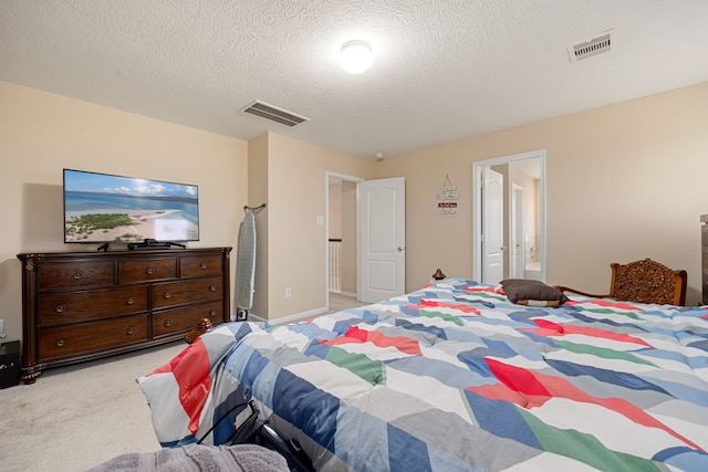 bedroom with light carpet, ensuite bathroom, and a textured ceiling