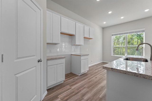 kitchen with white cabinetry, sink, light stone counters, and light hardwood / wood-style flooring