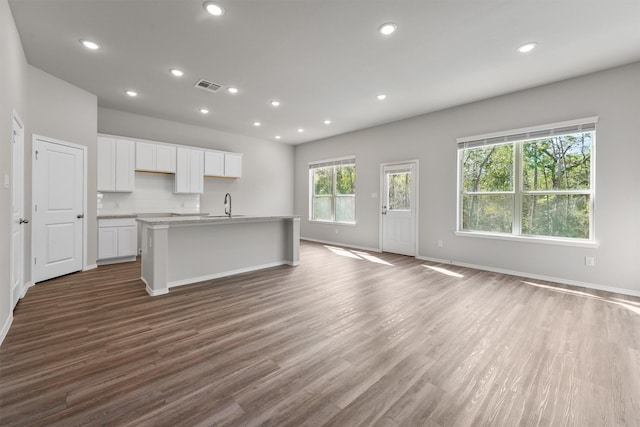 kitchen with tasteful backsplash, sink, dark hardwood / wood-style floors, white cabinetry, and an island with sink