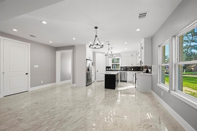 kitchen featuring a center island, backsplash, decorative light fixtures, white cabinets, and appliances with stainless steel finishes