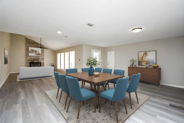 dining room with hardwood / wood-style flooring, vaulted ceiling, and a fireplace