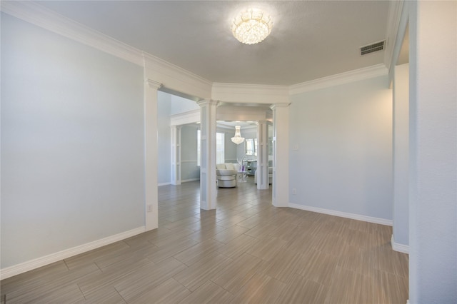 empty room featuring decorative columns, hardwood / wood-style floors, ornamental molding, and an inviting chandelier