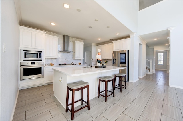 kitchen featuring white cabinetry, wall chimney exhaust hood, an island with sink, and appliances with stainless steel finishes