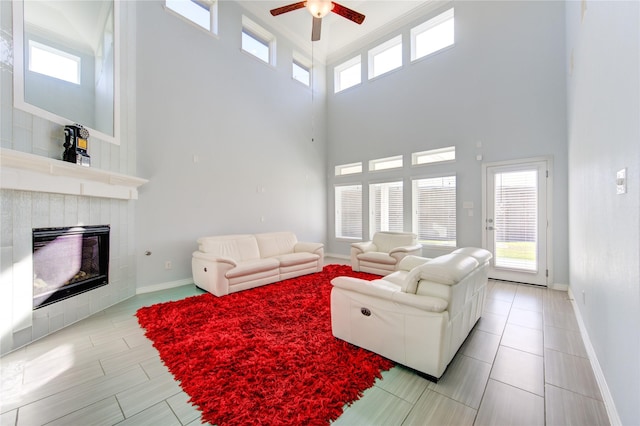 living room featuring a tile fireplace, ceiling fan, and a high ceiling