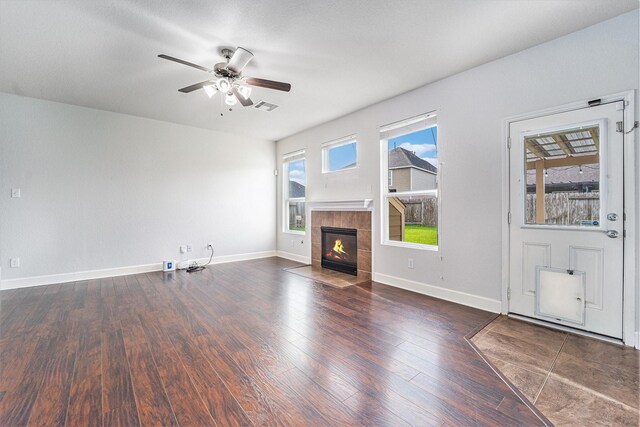 unfurnished living room featuring a tiled fireplace, ceiling fan, and dark hardwood / wood-style floors