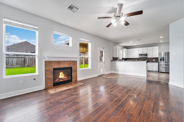 unfurnished living room with ceiling fan, a wealth of natural light, a tile fireplace, and dark hardwood / wood-style flooring