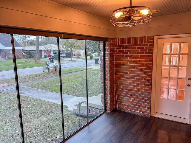 doorway to outside with dark hardwood / wood-style flooring, brick wall, plenty of natural light, and an inviting chandelier