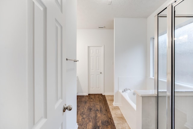 bathroom with independent shower and bath, wood-type flooring, and a textured ceiling