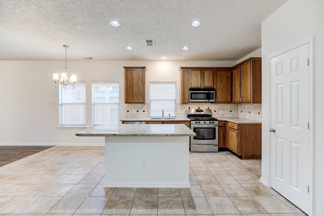 kitchen with decorative backsplash, appliances with stainless steel finishes, light stone counters, a notable chandelier, and hanging light fixtures