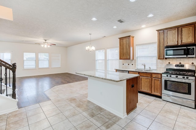 kitchen with light stone countertops, appliances with stainless steel finishes, ceiling fan with notable chandelier, sink, and light hardwood / wood-style floors