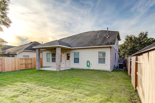 back house at dusk with ceiling fan, a patio area, central air condition unit, and a yard