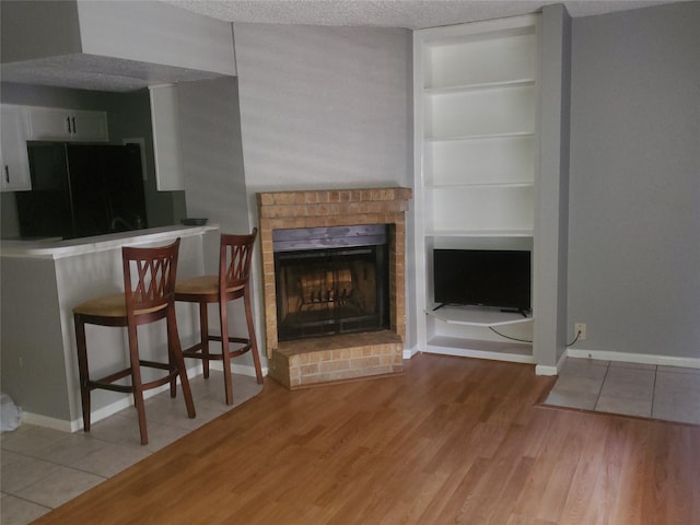 unfurnished living room with light hardwood / wood-style flooring, a textured ceiling, and a brick fireplace