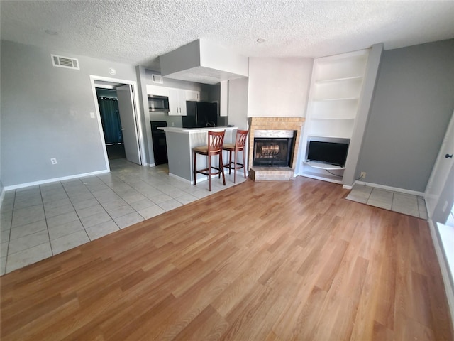 unfurnished living room featuring built in shelves, a brick fireplace, a textured ceiling, and light wood-type flooring