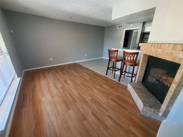 unfurnished living room with a brick fireplace, a textured ceiling, and light hardwood / wood-style flooring