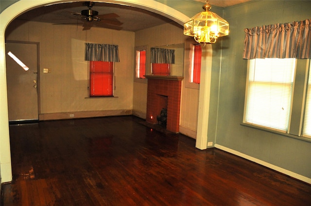 empty room featuring wood-type flooring, ceiling fan with notable chandelier, and a brick fireplace